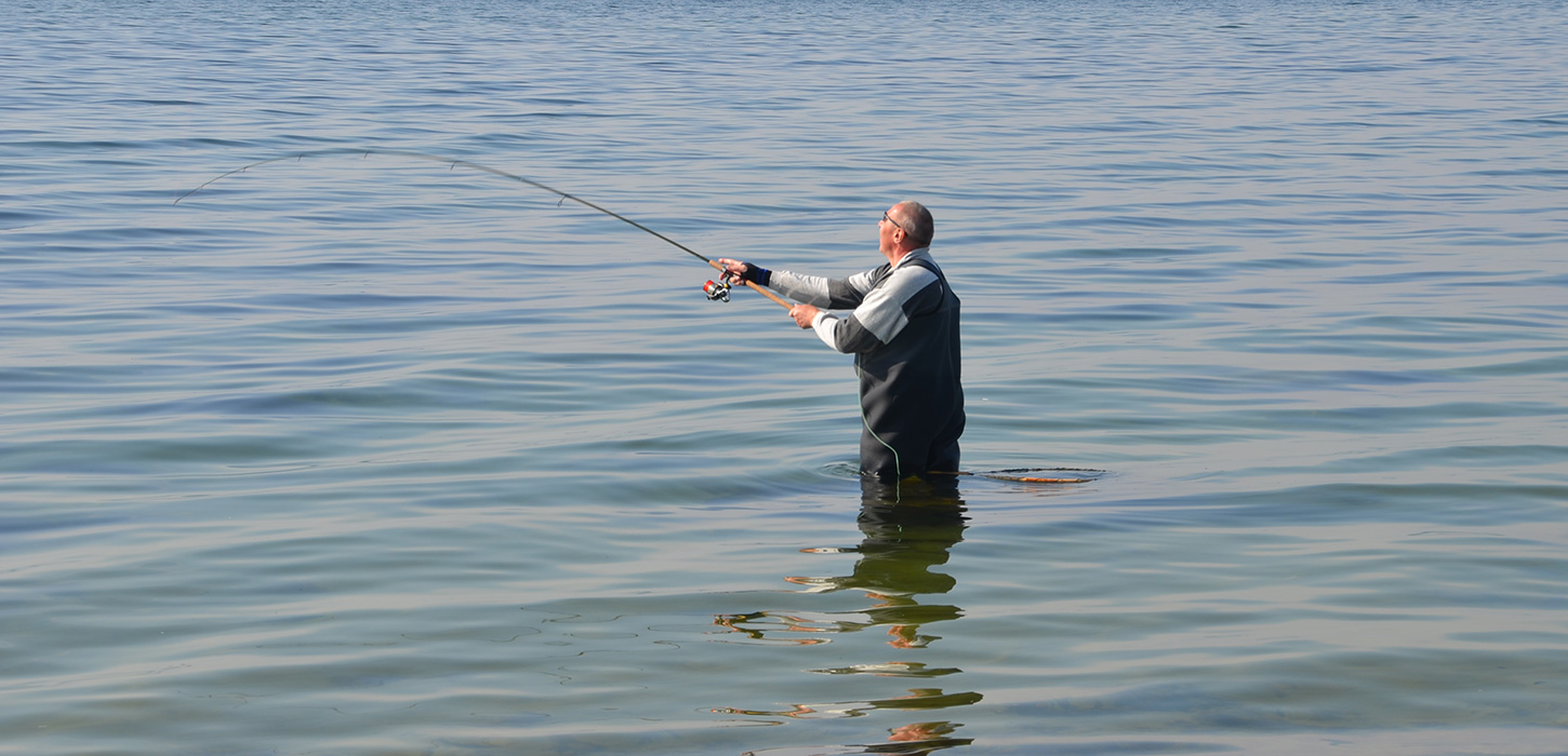 Lystfisker står alene i stille vand på Langeland og fisker med sin fiskestang