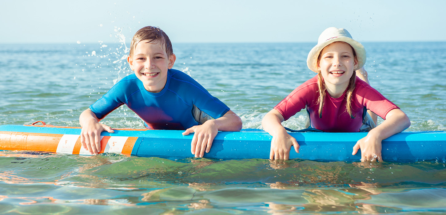 To børn ligger i vandet på et surfboard